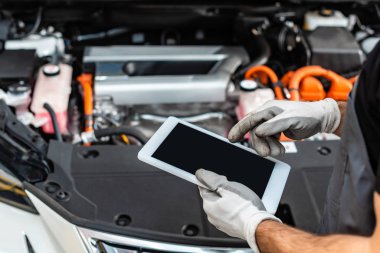 Otomobil motoru kompartımanının yanında dijital tablet kullanan tamircinin kırpılmış görüntüsü