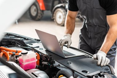 Araba motoru kompartımanının yanında dizüstü bilgisayar kullanan tamircinin kırpılmış görüntüsü