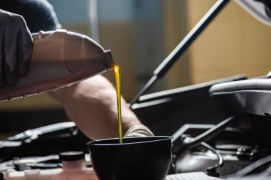 partial view of mechanic pouring motor oil at car engine clipart