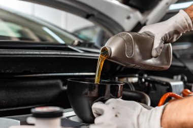 partial view of mechanic pouring motor oil at car engine clipart