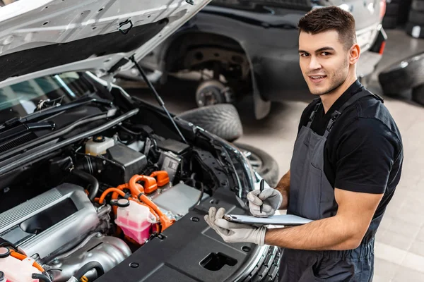 Escritura Mecánica Guapo Portapapeles Mientras Inspecciona Compartimiento Del Motor Del — Foto de Stock