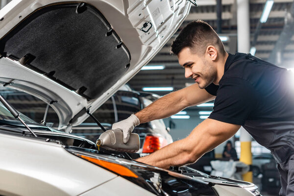 smiling mechanic pouring motor oil at car engine