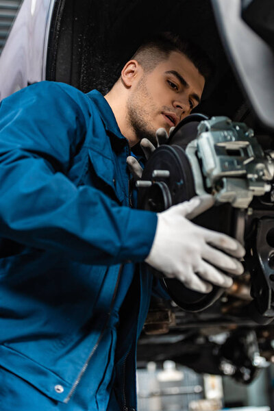 young, concentrated mechanic installing disc brakes on raised car