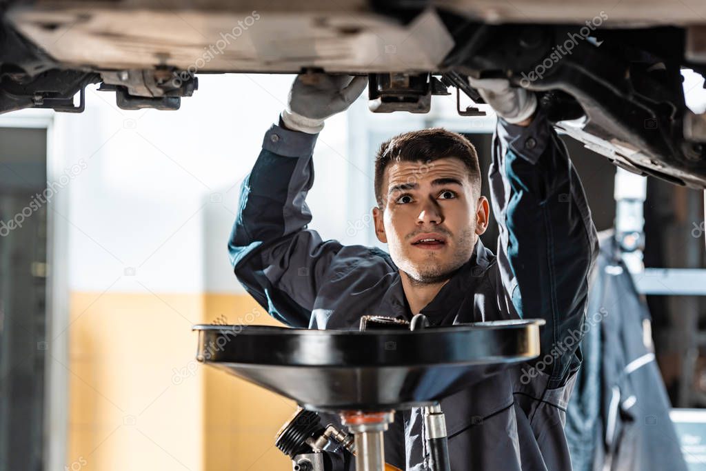 young mechanic looking at bottom of car near lube oil extractor