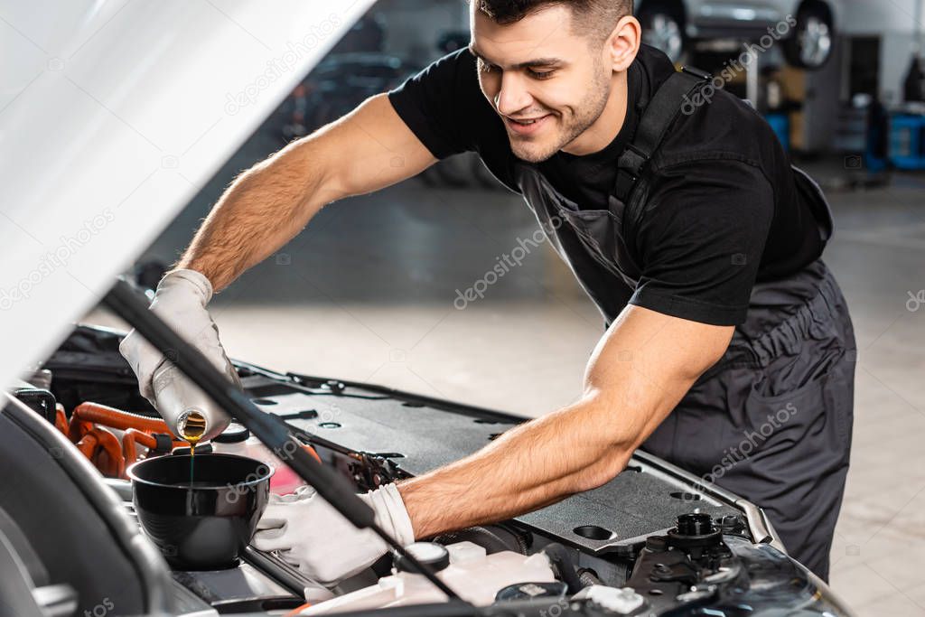 selective focus of smiling mechanic pouring oil to car engine
