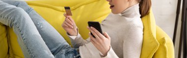 Kanepede kredi kartı ve akıllı telefon taşıyan bir kadının görüntüsü. 
