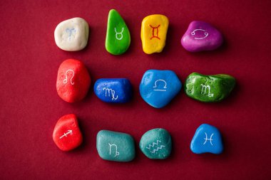 Top view of colorful stones with zodiac signs on red surface clipart