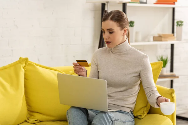 Menina Atraente Segurando Cartão Crédito Xícara Café Usar Laptop Sofá — Fotografia de Stock