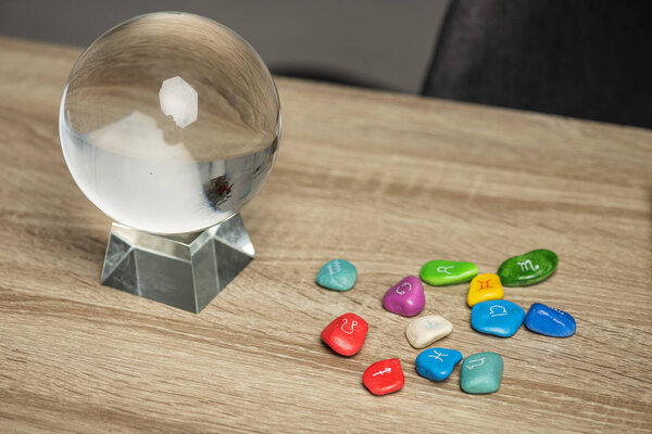 Crystal ball and colorful stones with zodiac signs on wooden table