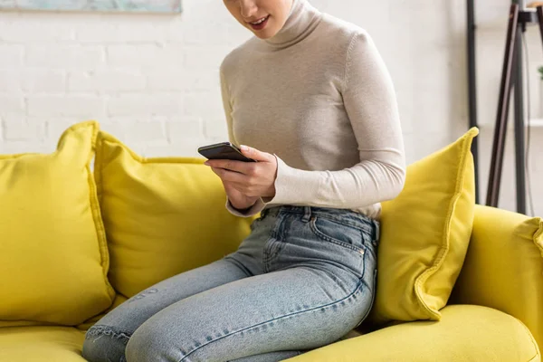 Beskuren Över Leende Flicka Som Håller Smartphone Soffan Hemma — Stockfoto