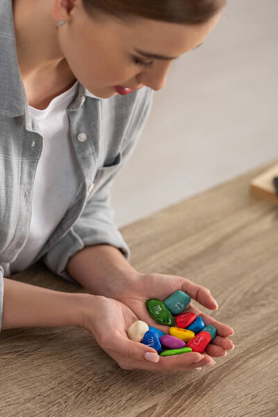 Selective focus of astrologer holding colorful stones with zodiac signs at table