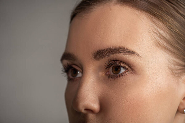 Обрезанный вид молодой женщины, смотрящей в сторону на сером фоне

