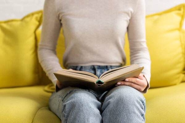 Cropped view of woman reading book on couch at home