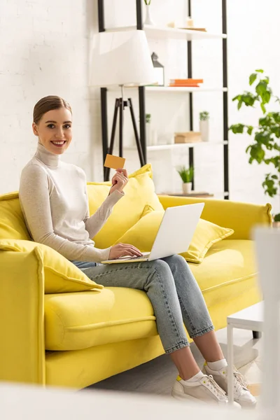 Woman Smiling Camera Showing Credit Card While Using Laptop Couch — Stock Photo, Image