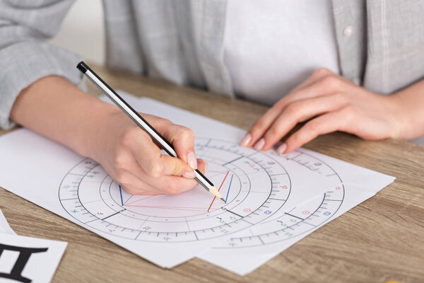 Cropped view of astrologer drawing natal chart on wooden table