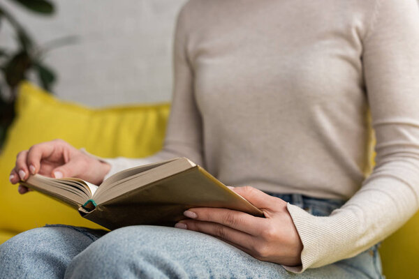 Cropped view of young woman reading book on couch