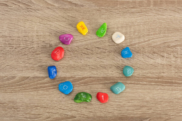 Top view of round frame with colorful stones with zodiac signs on wooden table
