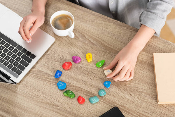 Вид сверху астролога с помощью камней со знаком зодиака и ноутбука рядом с кофе на столе, обрезной вид
