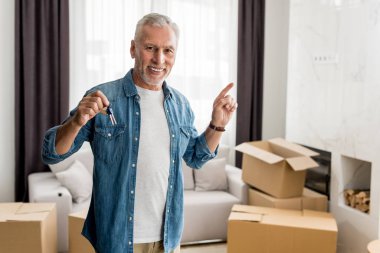smiling man holding keys and pointing with finger in new house  clipart