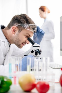 selective focus of smiling molecular nutritionist using microscope in lab  clipart