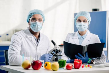 Tıbbi maskeli moleküler beslenme uzmanları laboratuvarda kameraya bakıyor.