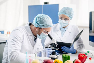 Moleküler beslenme uzmanı elinde klasör tutuyor ve mikroskopla meslektaşına bakıyor.