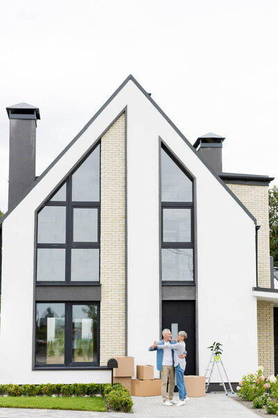 mature man and smiling woman dancing and looking at each other near new house 
