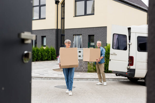 mature man and smiling woman bringing boxes to new house 