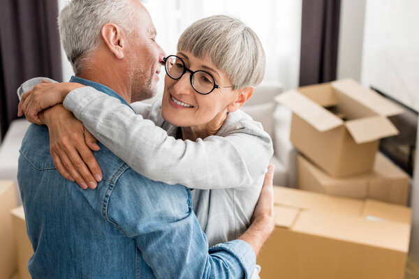 smiling woman in glasses hugging mature man in new house 