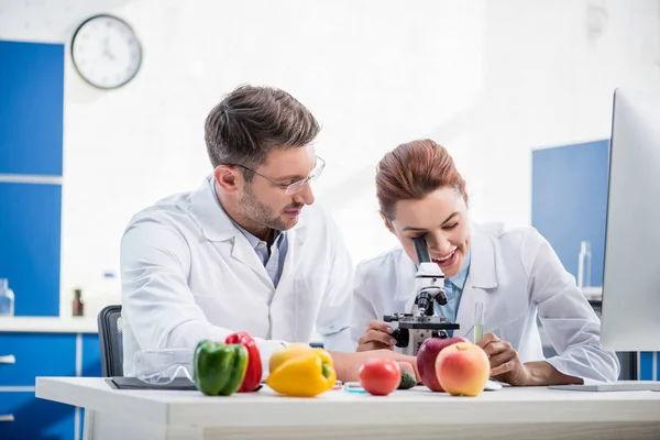 Sorrindo Nutricionista Molecular Usando Microscópio Seu Colega Olhando Para Ela — Fotografia de Stock