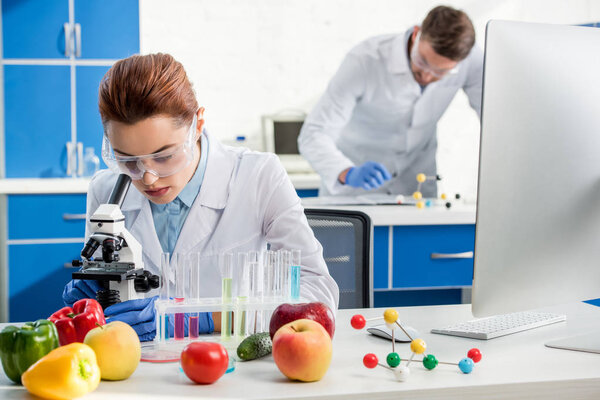selective focus of molecular nutritionist using microscope and colleague on background 