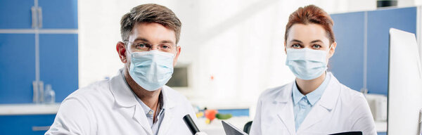 panoramic shot of molecular nutritionists in medical masks looking at camera 