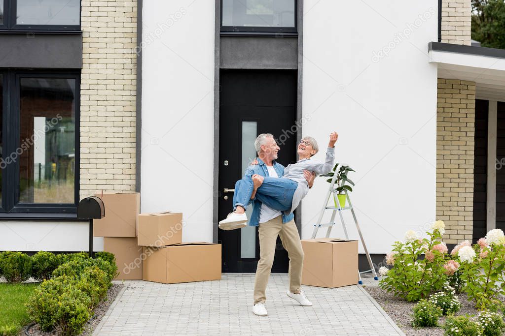 handsome mature man holding smiling woman near new house 