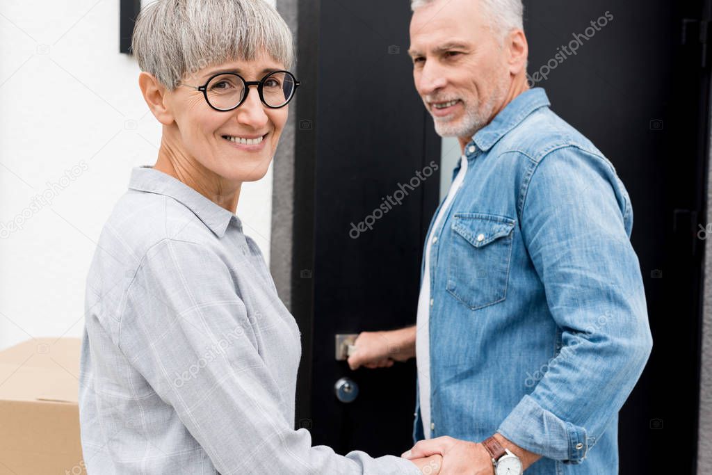 mature man looking at smiling woman and entering to new house 