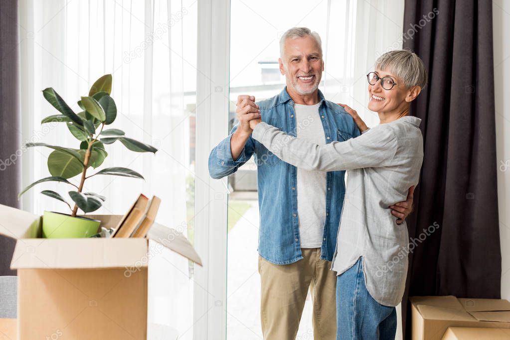 mature man and smiling woman dancing in new house 