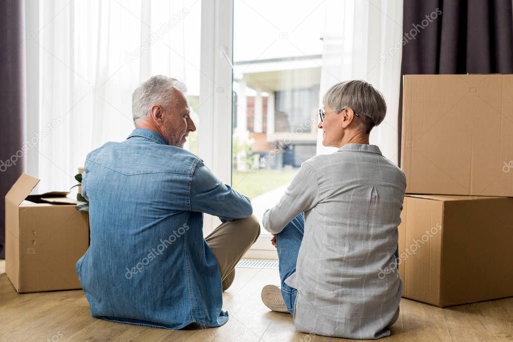 back view of mature man and woman sitting on floor in new house 