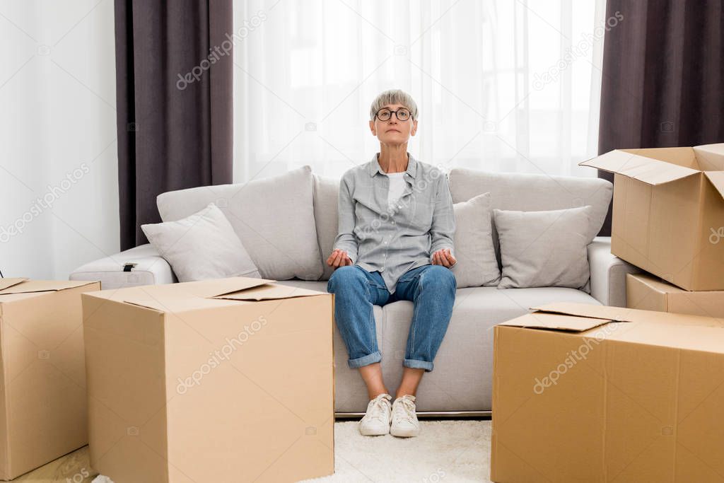 mature woman sitting on sofa and meditating in new house 