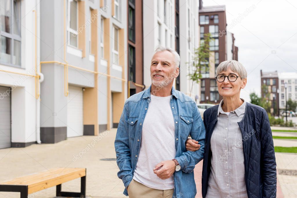mature man and smiling woman walking near new houses 