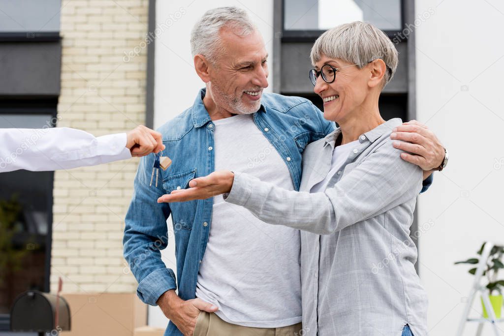 cropped view of broker giving keys of new house to smiling man and woman 