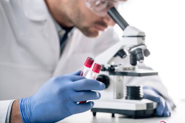 Genetik danışmanın elinde test tüpleri tutarken mikroskop kullanırken... 