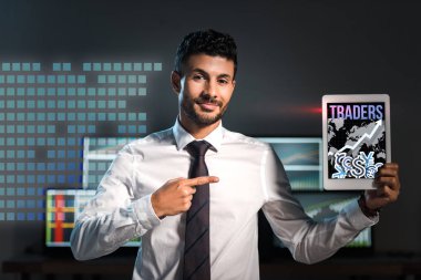 happy bi-racial man pointing with finger at digital tablet with traders letters on screen clipart