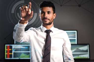 selective focus of handsome bi-racial trader pointing with finger near computers on background  clipart