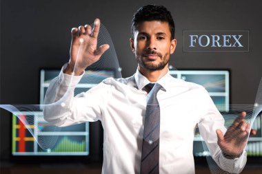 selective focus of bi-racial trader pointing with fingers near computers and forex letters clipart
