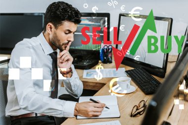 Düşünceli iki ırklı tüccar deftere yazı yazıyor ve masanın yanında oturuyor. Satıp mektup alıyor.
