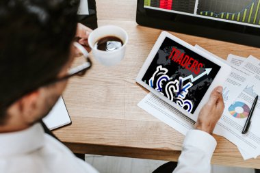 selective focus of man holding cup and digital tablet with traders letters  clipart