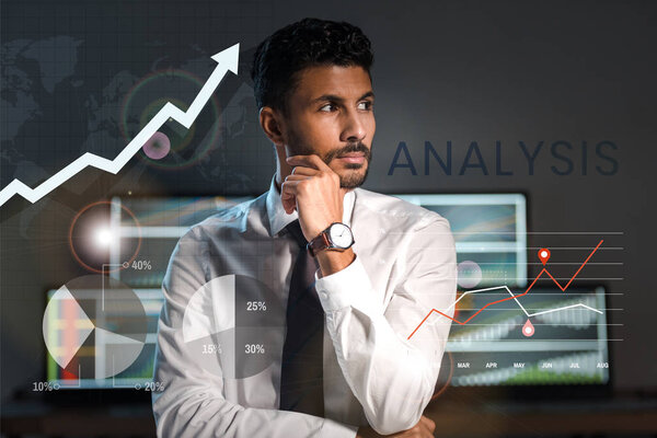 pensive bi-racial trader looking away near charts, graphs and letters in office 