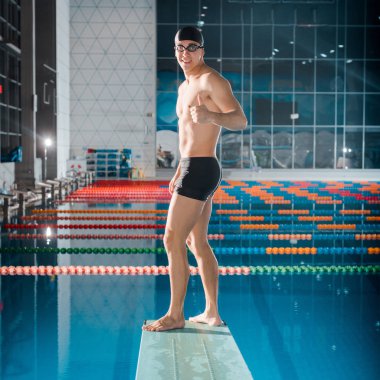 smiling swimmer showing thumb up while standing on diving board  clipart