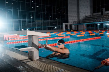 Gözlüklü yakışıklı yüzücü yüzme havuzunda egzersiz yapıyor. 