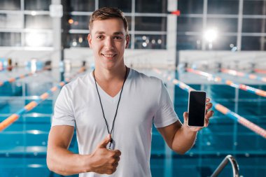 Mutlu antrenör boş ekranla akıllı telefonu tutarken baş parmağını gösteriyor 