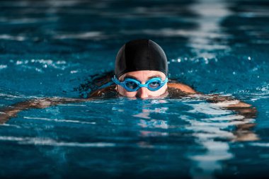 selective focus of athletic man in goggles training in swimming pool  clipart